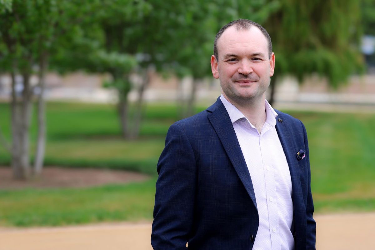 Jamie Lewis in a blue and purple suit looks to the camera with grassed area in the background