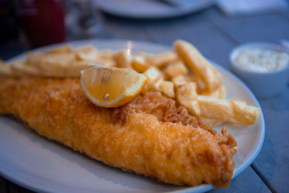 A traditional portion of battered fish and chips, often with cod, haddock and plaice with potato chips and a slice of lemon, salt and vinegar on a large plate .