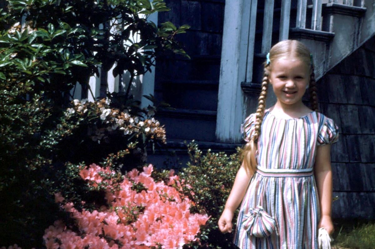 Susan Walton in her garden as a child, next to an azelea bush
