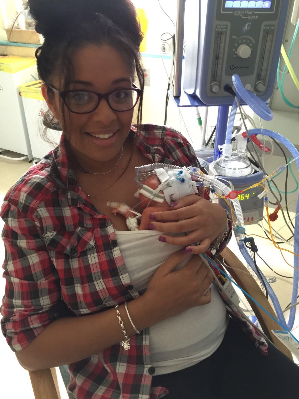 Roxanne Cooper holds her baby underneath her shirt and smiles to the camera after he was born 23 weeks early