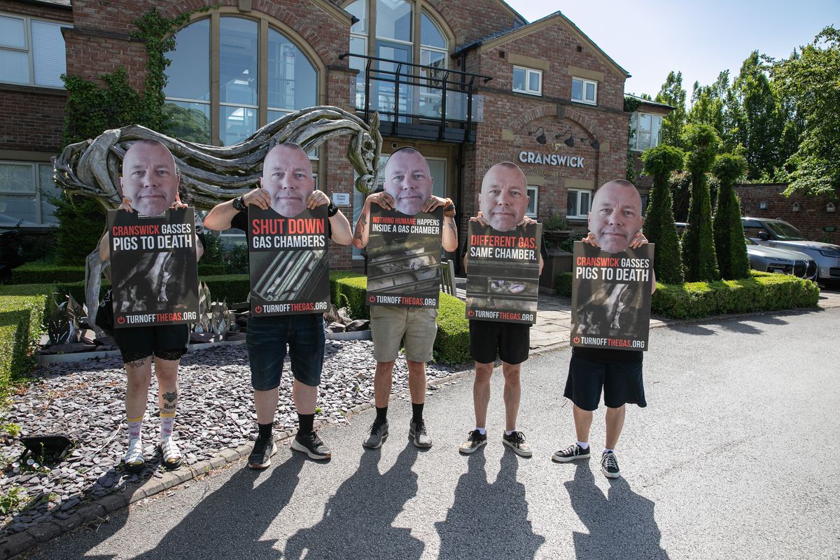 Protestors hold up masks depicting the face of Adam Couch
