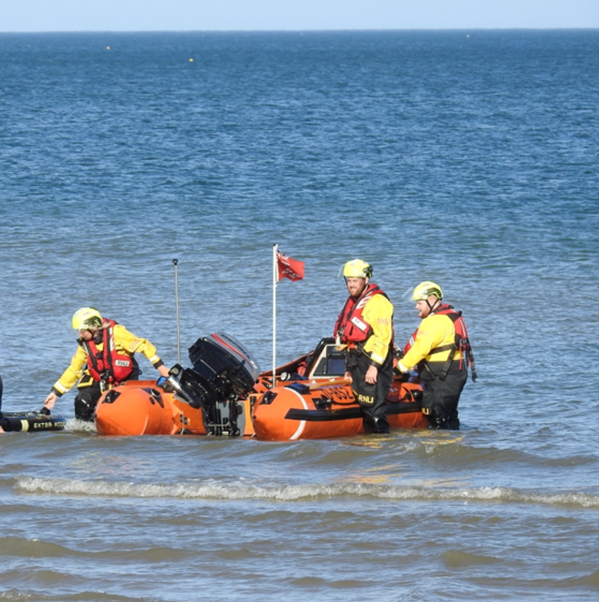 Members of the volunteer RNLI crew in shallow water on the lifeboat after returning the paddleboarder to the beach