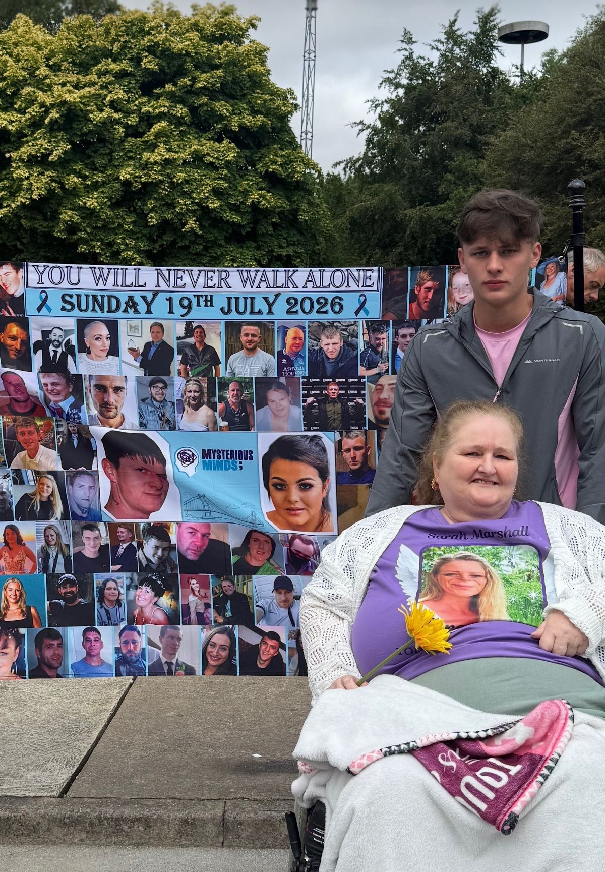 Jayden Swallow, Jayne's grandson, stands with his grandmother and a banner in memory of those who have taken their own lives in Hull