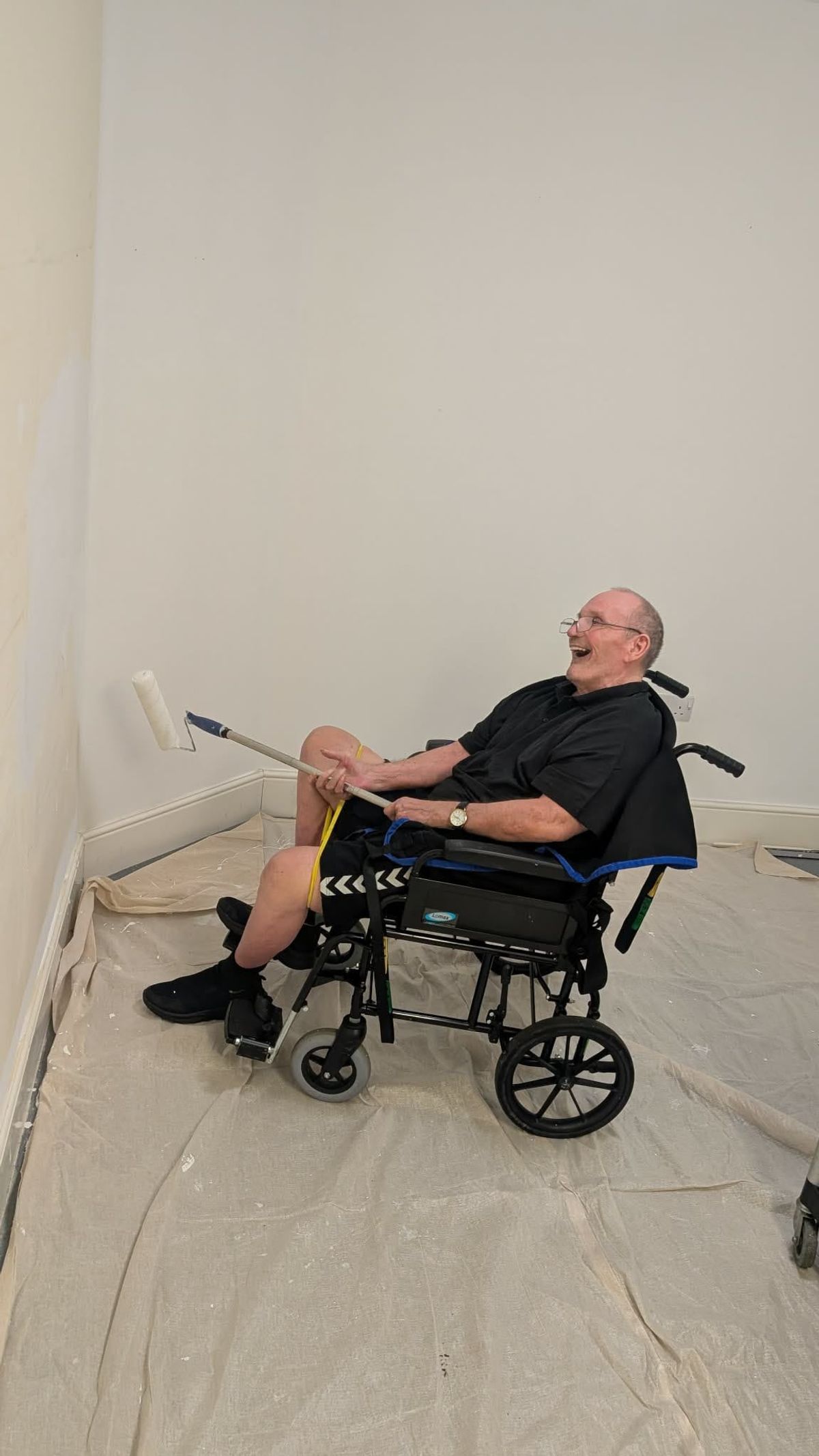 Bob McKenna painting a wall in his wheelchair using a roller brush