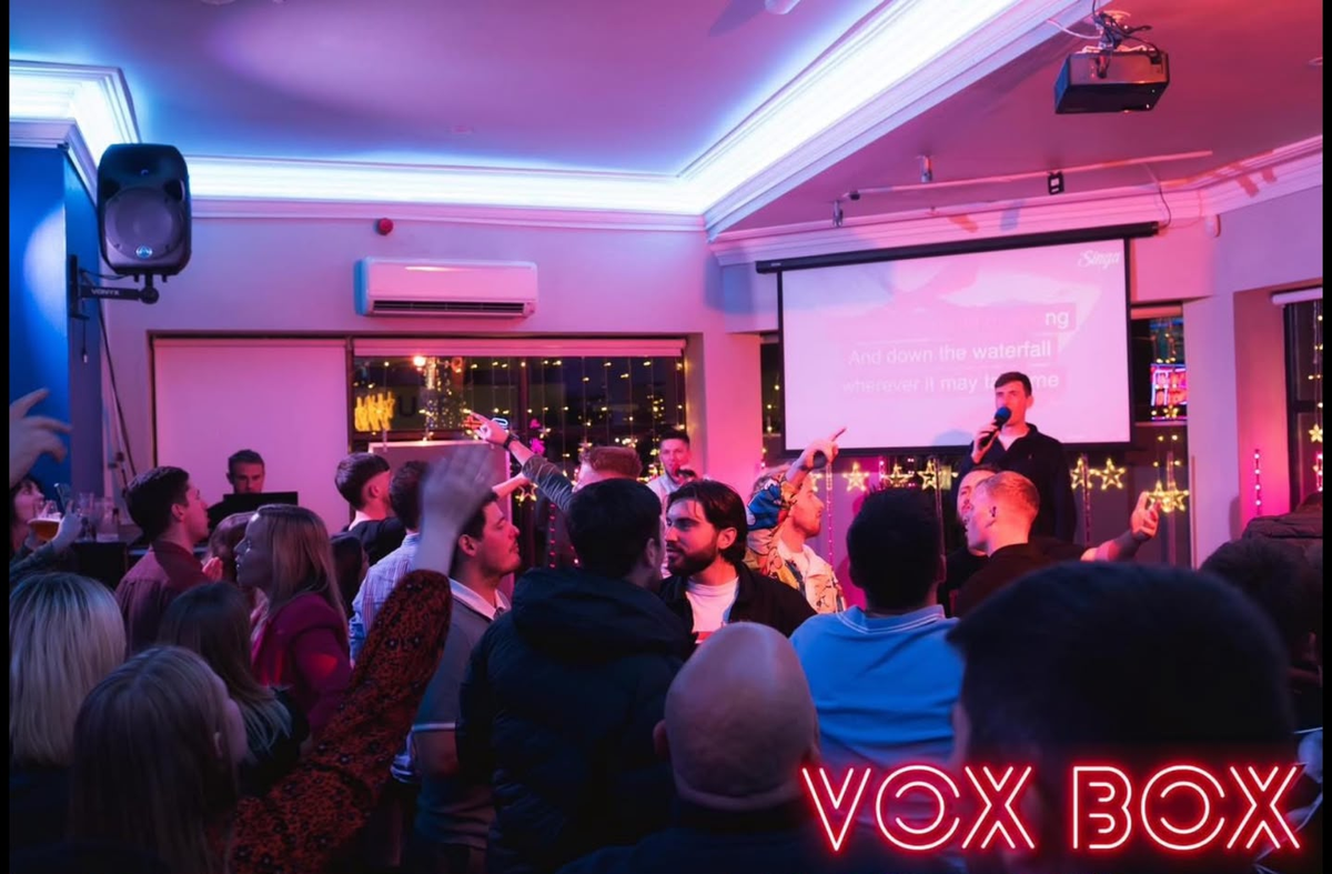 A full room view of the former Vox Box, with a man singing karaoke and the rest of the room of revellers singing along 