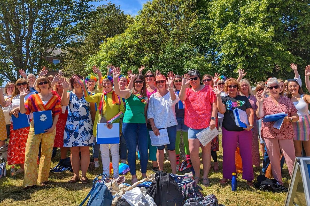 A group shot of one of Lucy's Pop Choirs with songbooks in an outdoor event